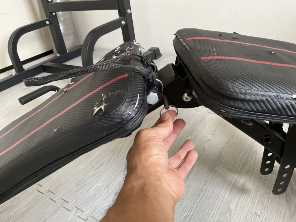 FLYBIRDトレーニングベンチを折りたたむ際に操作する、ヒンジ部分の固定用リングピンを引っ張る様子。