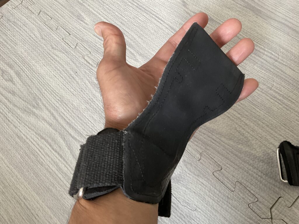 左手に装着したHiseason(ハイシーズン)の握力補助用パワーグリップ。手のひら側のベロ部分と、手首を固定するベルクロストラップのアップ画像。